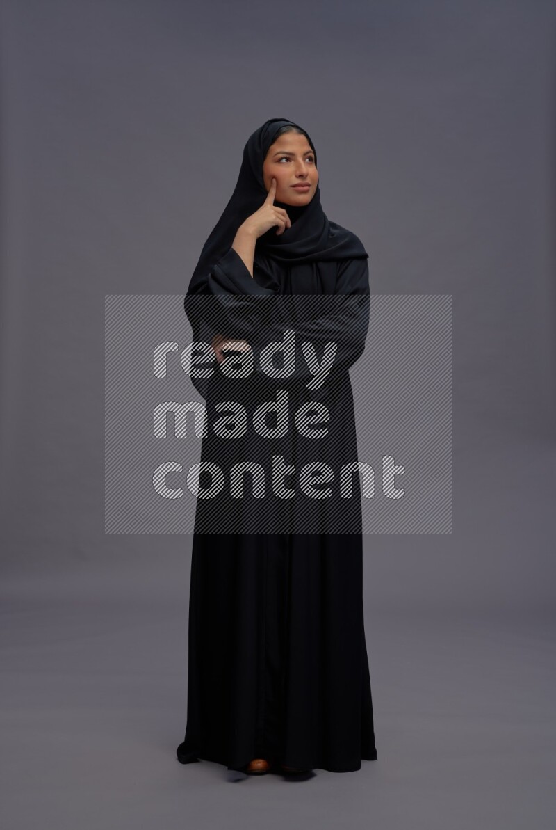 Saudi woman wearing Abaya standing interacting with the camera on gray background