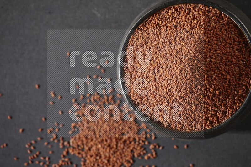 A black pottery bowl full of garden cress seeds on a black flooring