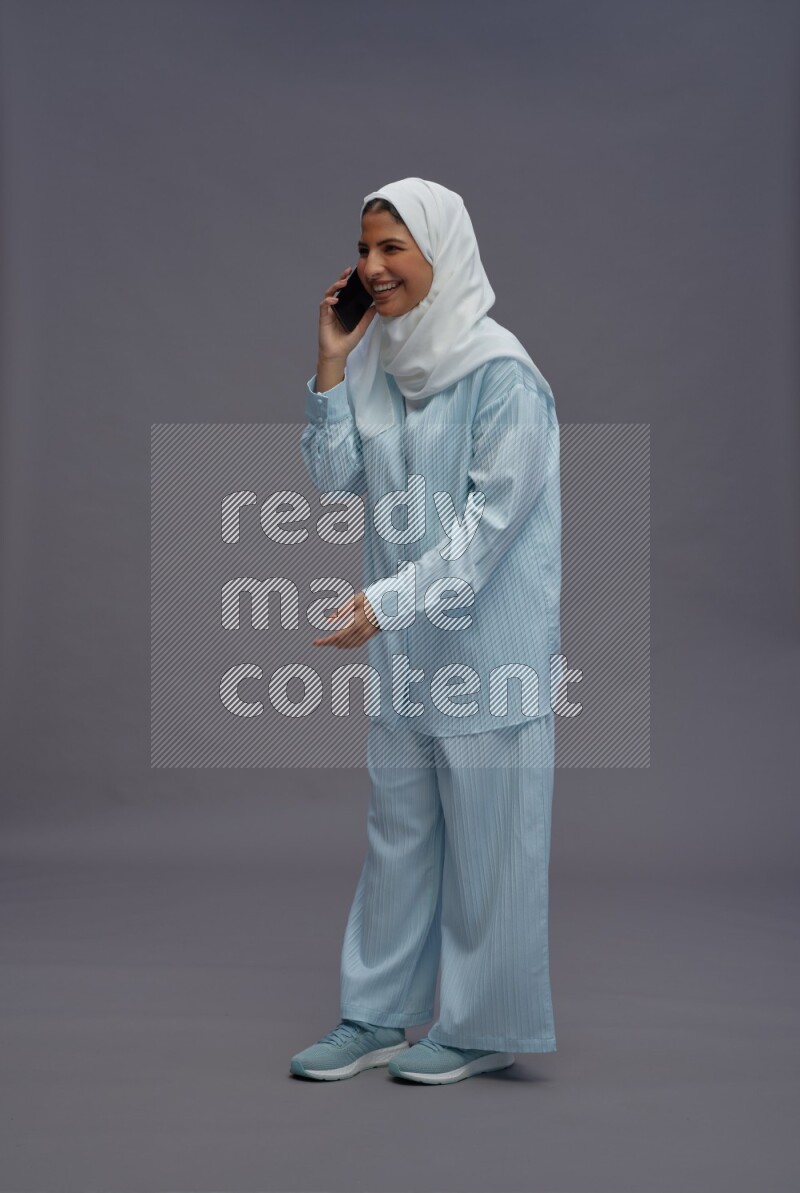 Saudi woman wearing hijab clothes standing talking on phone on gray background