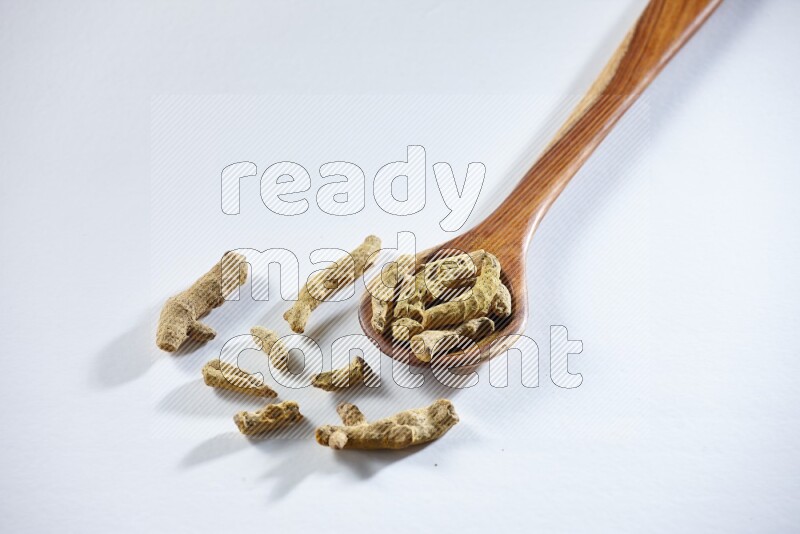 A wooden ladle full of dried turmeric fingers on white flooring
