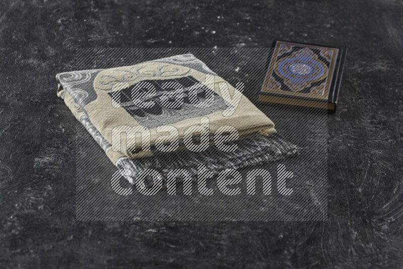 A folded prayer mat with different elements such as quran and prayer beads on black textured background