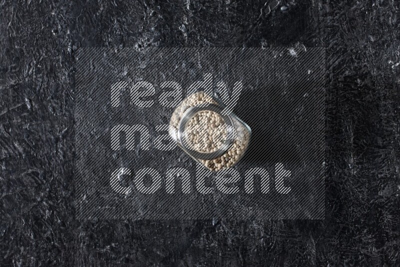 Herbal glass jar full of white pepper on textured black flooring