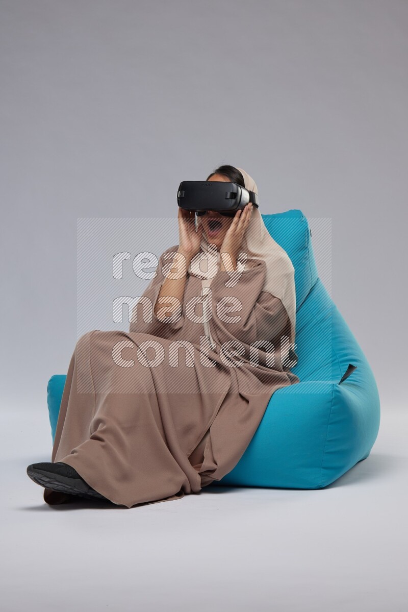 A Saudi woman sitting on a blue beanbag and gaming with VR