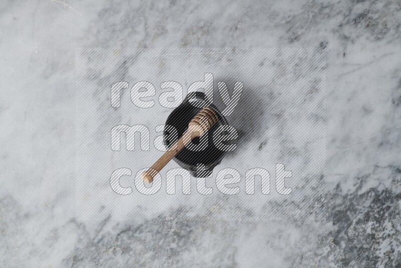 Black pottery bowl with wooden honey dipper in it on grey marble background