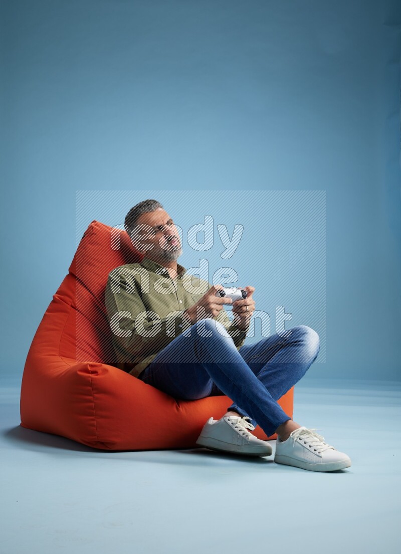 A man sitting on an orange beanbag and gaming with joystick