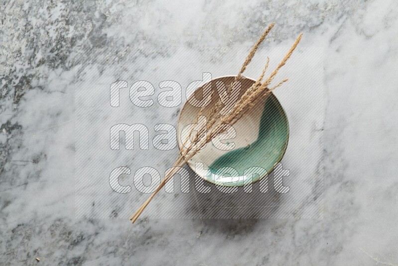 Wheat stalks on multicolored pottery plate on grey marble background