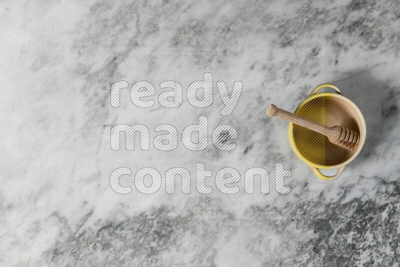 وعاء فخاري متعدد الألوان مع ملعقة عسل خشبية بداخله على خلفية من الرخام الرمادي