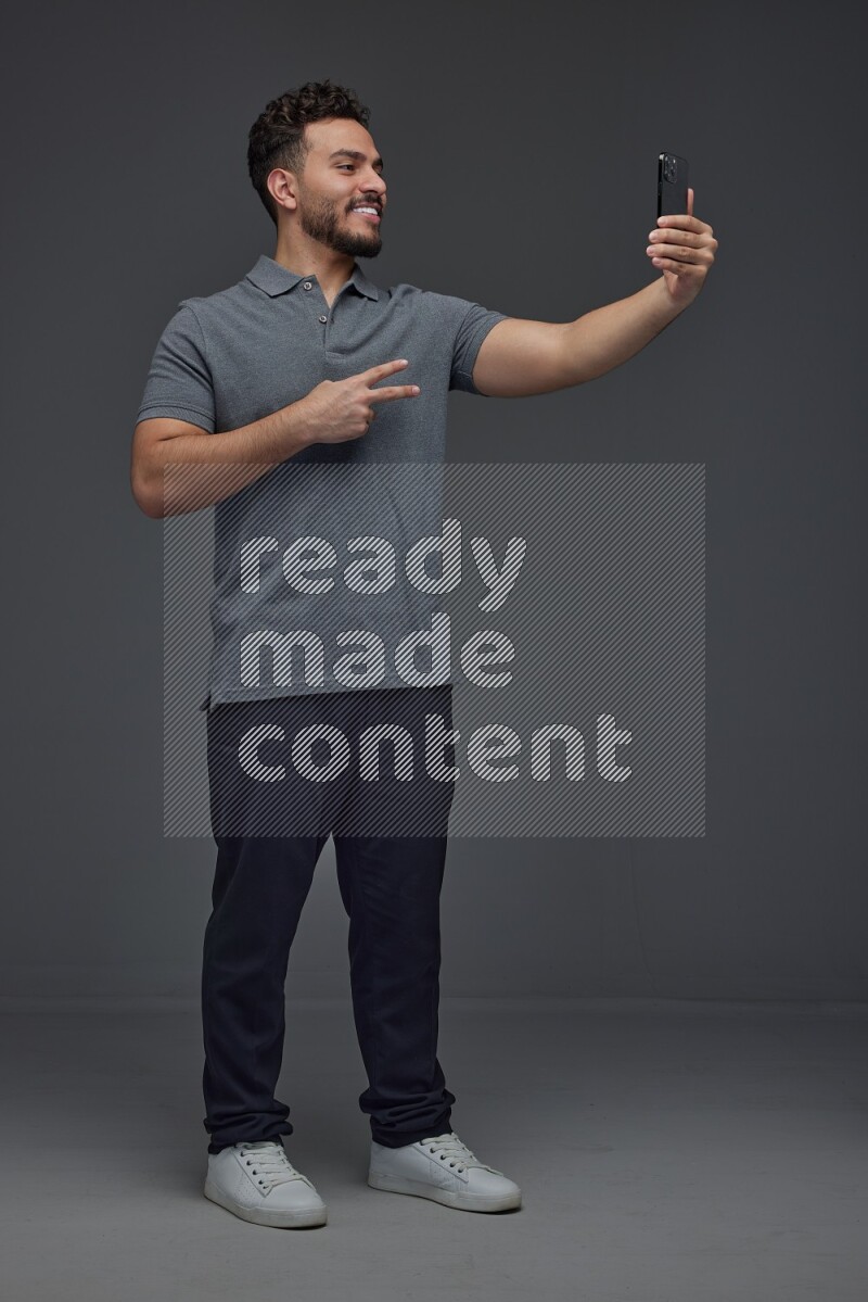 A man wearing casual and taking selfie with his phone different angles eye level on a gray background