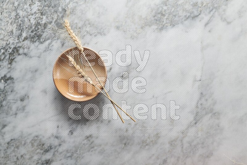 Wheat stalks on multicolored pottery plate on grey marble background
