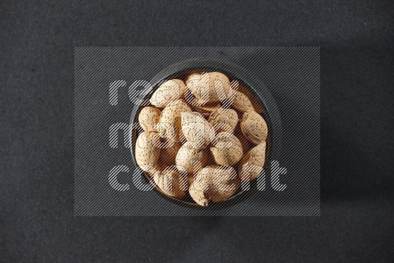 A black pottery bowl full of almonds on a black background in different angles