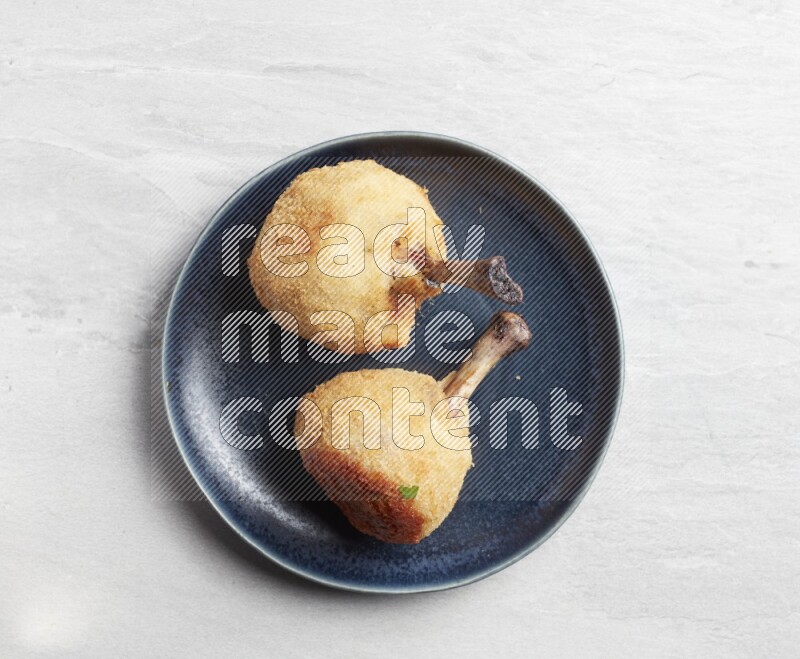 breaded drumstick on round dark grey pottery plate on grey textured countertop