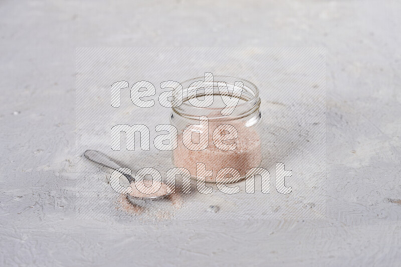 A glass jar full of fine himalayan salt on white background