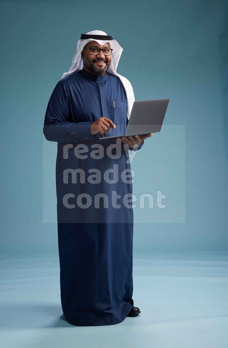 Saudi Man with shimag Standing working on laptop on blue background