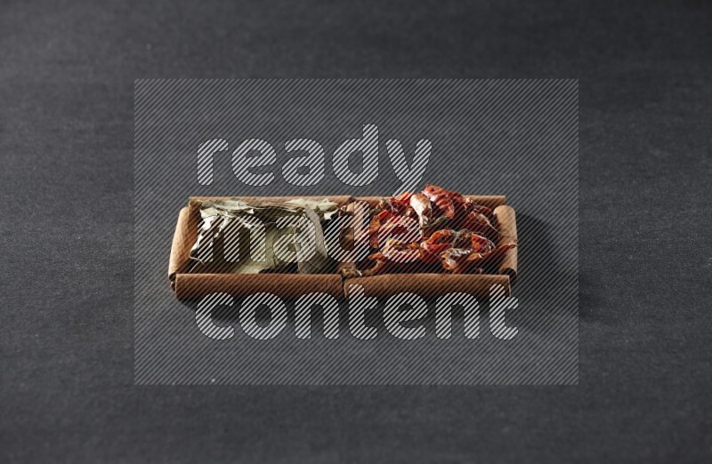 مربعان من أعواد القرفة ممتلئان بالفلفل الحار المجفف وأوراق الغار علي خلفية سوداء