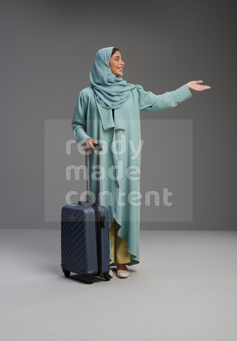 Saudi Woman wearing Abaya standing holding Travel bag on Gray background