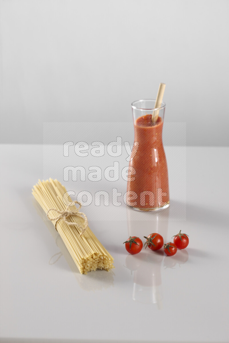 Raw pasta with tomatoe pasta with different ingredients such as cherry tomatoes, basil, garlic, bay laurel, cardamom, white pepper, black pepper, red chilis and wheat stalks on light grey background