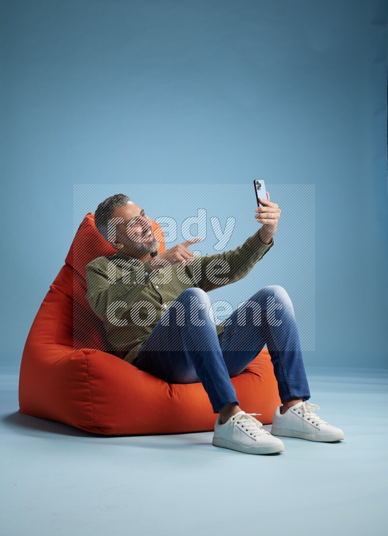 A man sitting on an orange beanbag and taking selfie