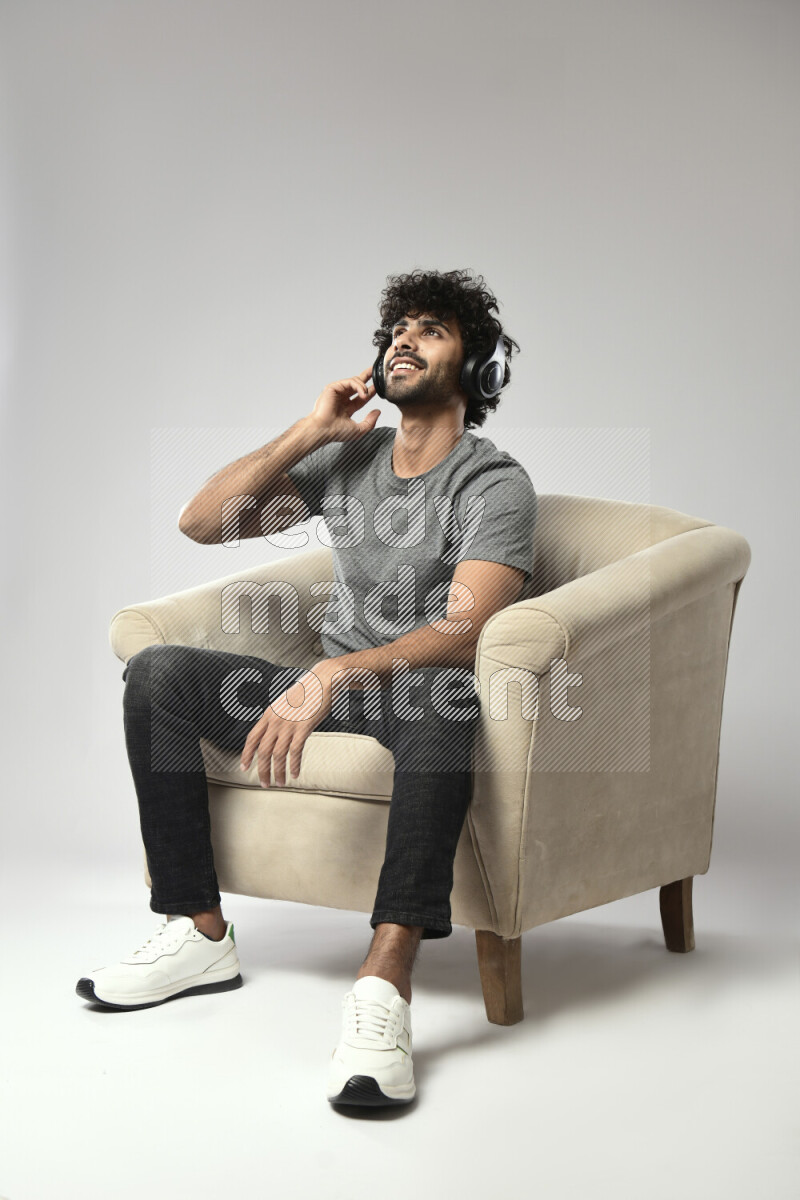 A man wearing casual sitting on a chair putting on headphones on white background