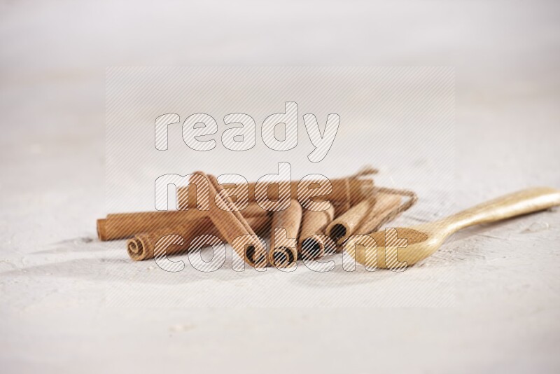 Cinnamon sticks stacked beside a wooden spoon full of cinnamon powder on white background