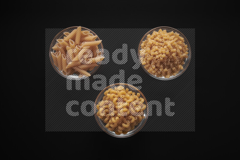 Different pasta types in glass bowls on black background
