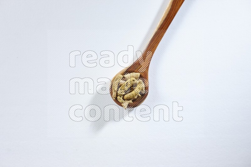 مغرفة خشبية مليئة بأصابع الكركم المجففة على خلفية بيضاء