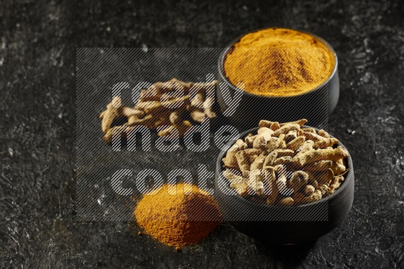 وعاءان من الفخار باللون الأسود، أحدهما ممتلئ ببودرة الكركم والآخر ممتلئ بأصابع كاملة من الكركم المجفف على خلفية سوداء