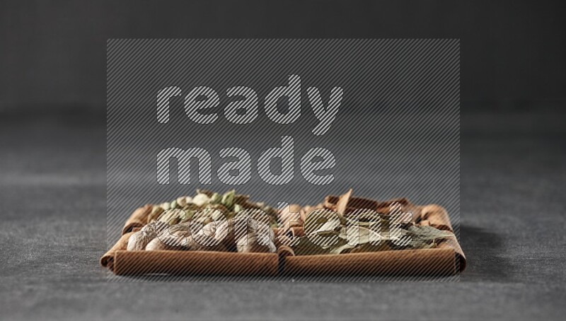 4 مربعات من عيدان القرفة ممتلئة بقطع القرفة وحبوب الهيل وأوراق الغار وجوزة الطيب على أرضية سوداء