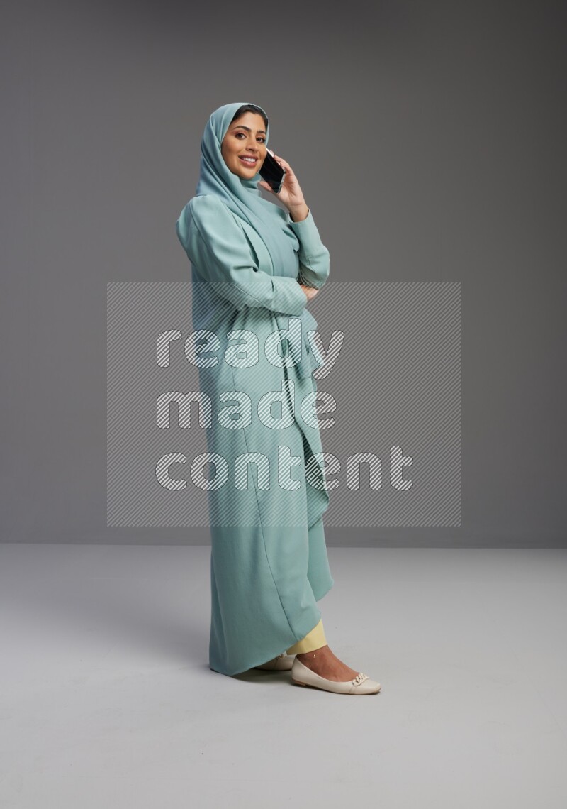Saudi Woman wearing Abaya standing talking on phone on Gray background