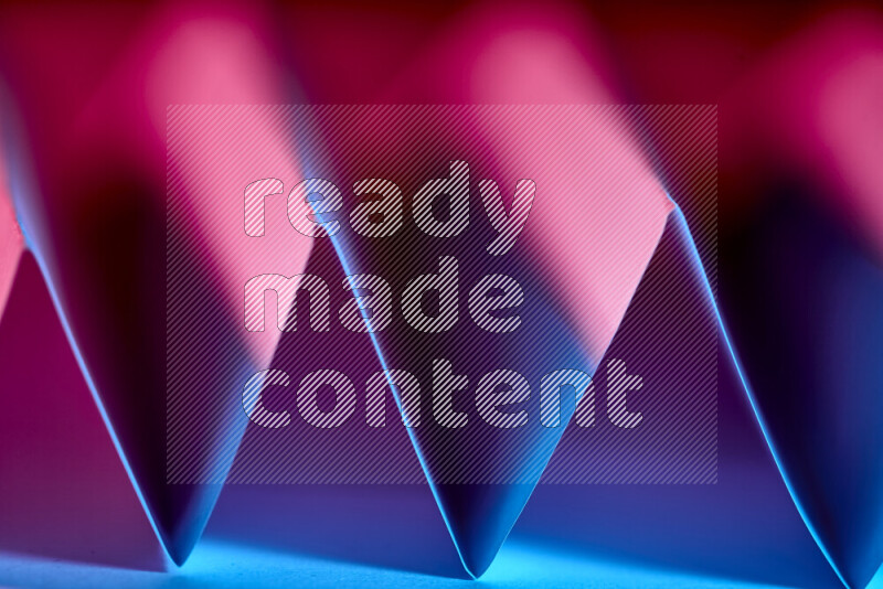 A close-up abstract image showing sharp geometric paper folds in blue and pink gradients