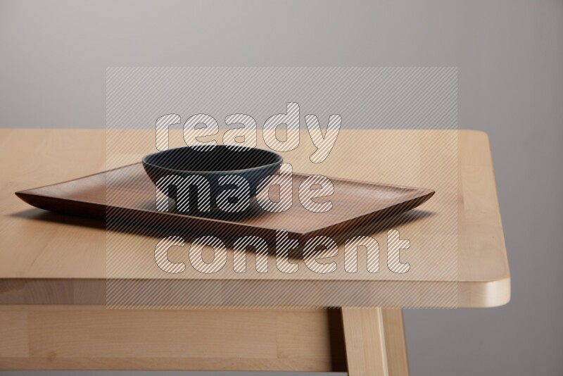 blue bowl placed on a rectangular wooden tray on the edge of wooden table