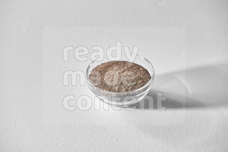 A glass bowl full of black pepper powder on white flooring