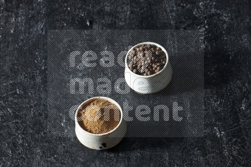 وعاءان بيج، أحدهما ممتلئ ببودرة بهار الفلفل الحلو والآخر بالحبوب على خلفية سوداء