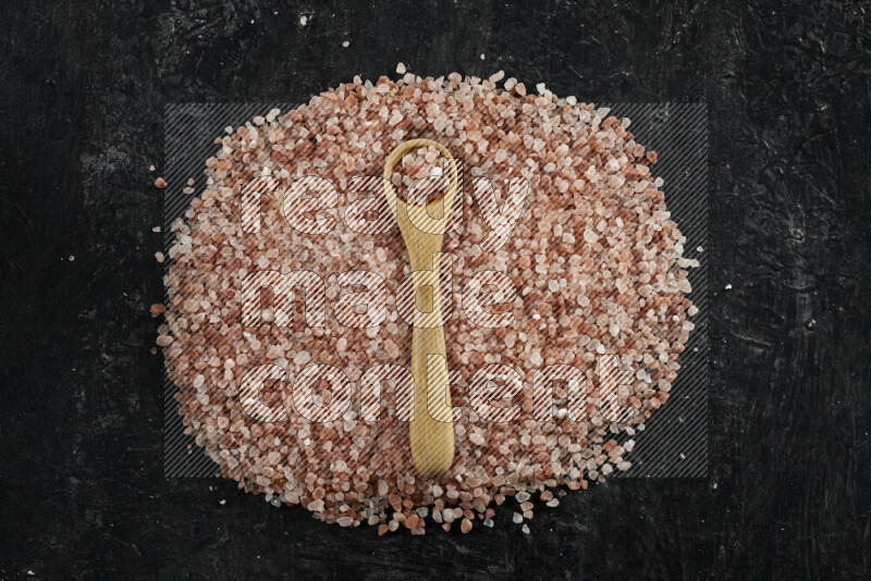 A wooden spoon full of coarse himalayan salt crystals on a bunch of the crystals on black background