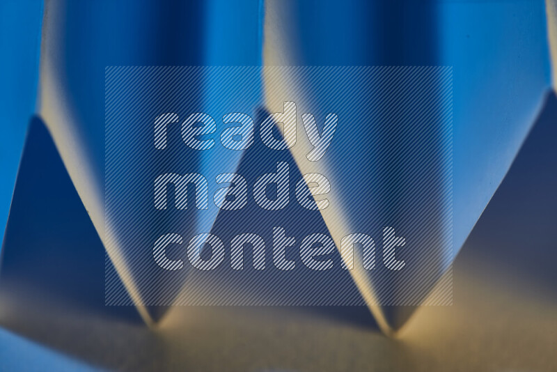 A close-up abstract image showing sharp geometric paper folds in blue gradients and warm tones