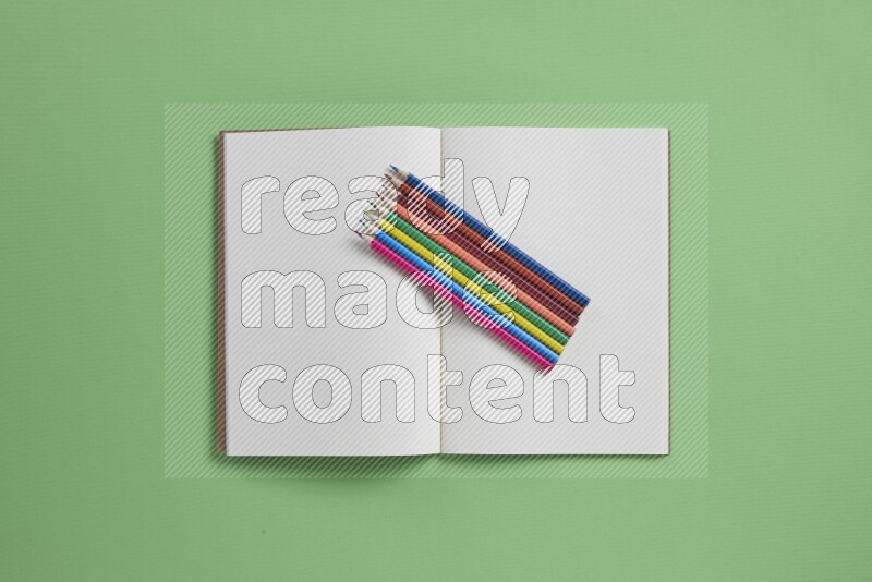 A blank open notebook with different school supplies on green background