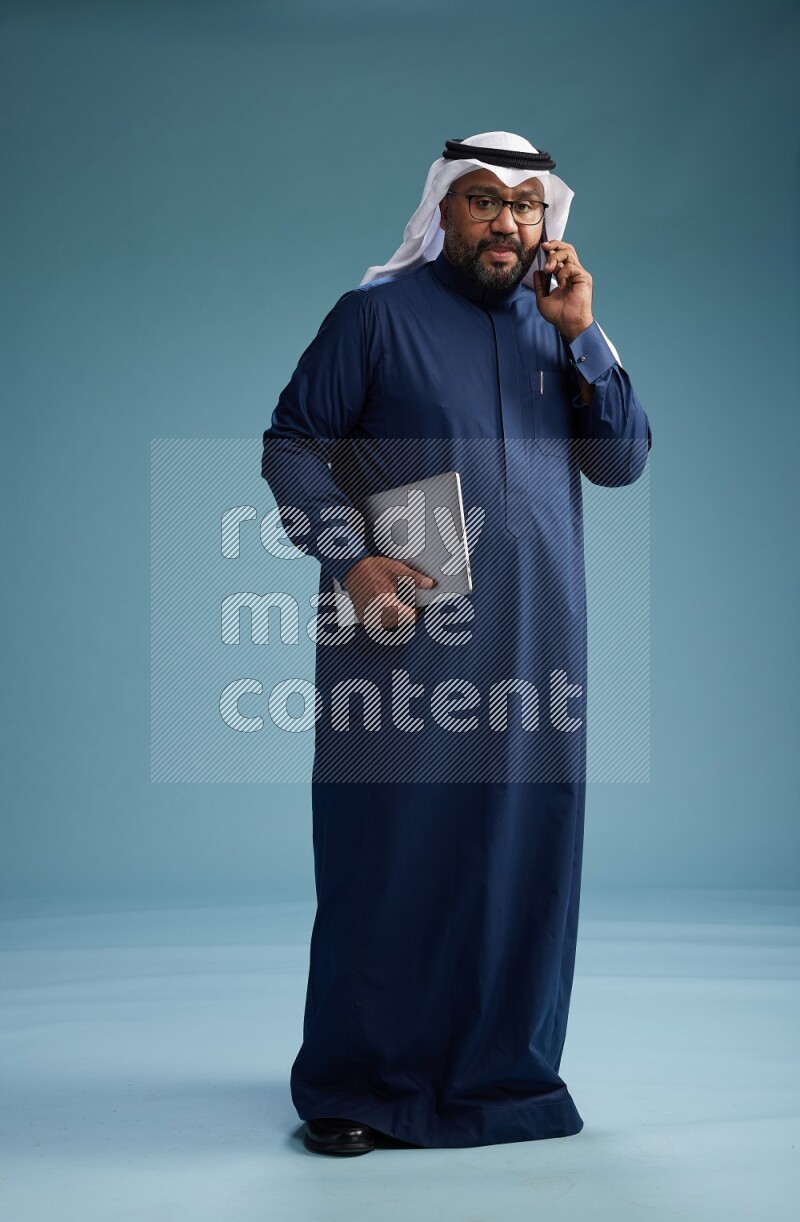Saudi Man with shimag Standing talking on phone on blue background