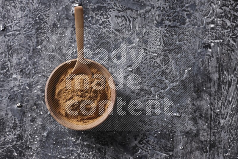 Wooden bowl full of cinnamon powder with a wooden spoon on a textured black background in different angles
