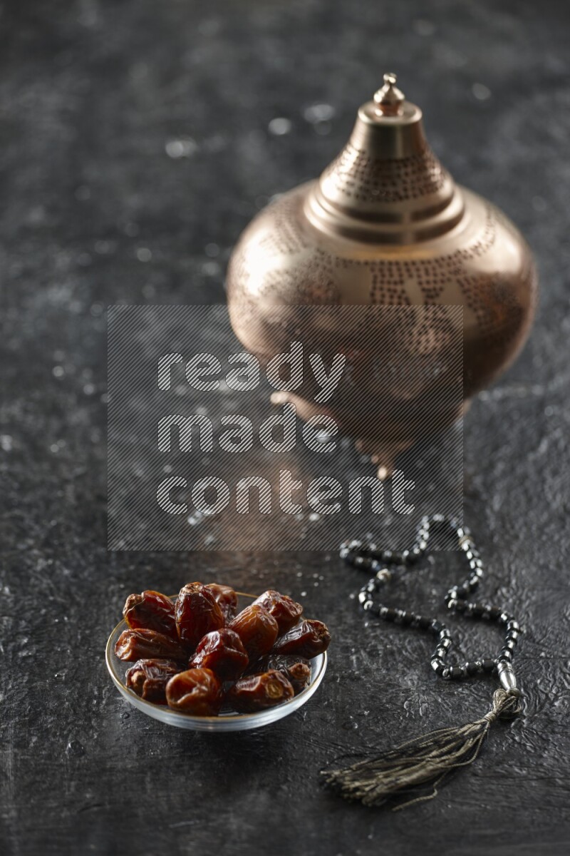 A golden lantern with different drinks, dates, nuts, prayer beads and quran on textured black background