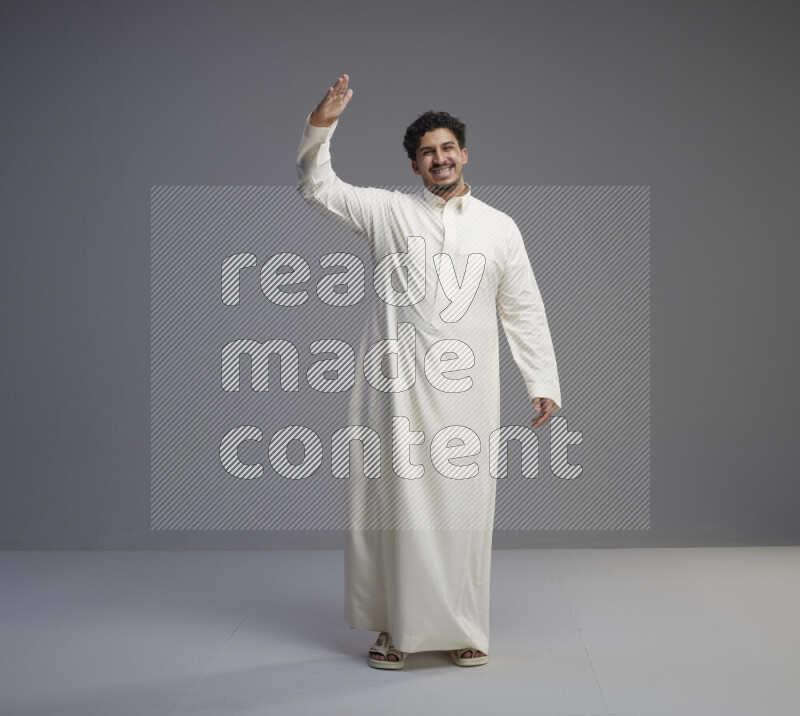 A Saudi man standing wearing thob interacting with the camera on gray background
