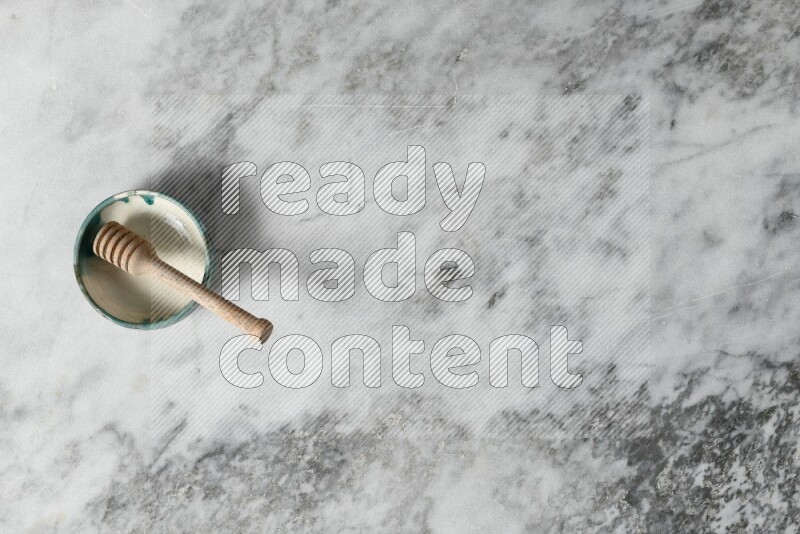 وعاء فخاري متعدد الألوان مع ملعقة عسل خشبية بداخله على خلفية من الرخام الرمادي