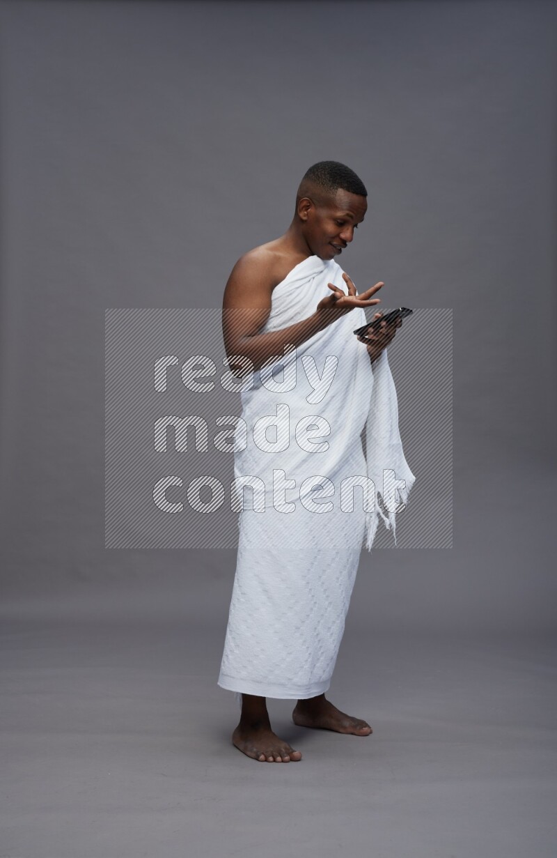 A man wearing Ehram Standing texting on phone on gray background