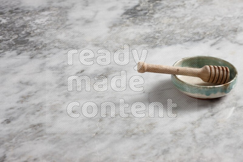 Multicolored pottery bowl with wooden honey dipper in it on grey marble background