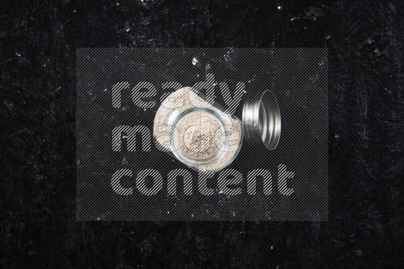 A glass jar full of onion powder on black background