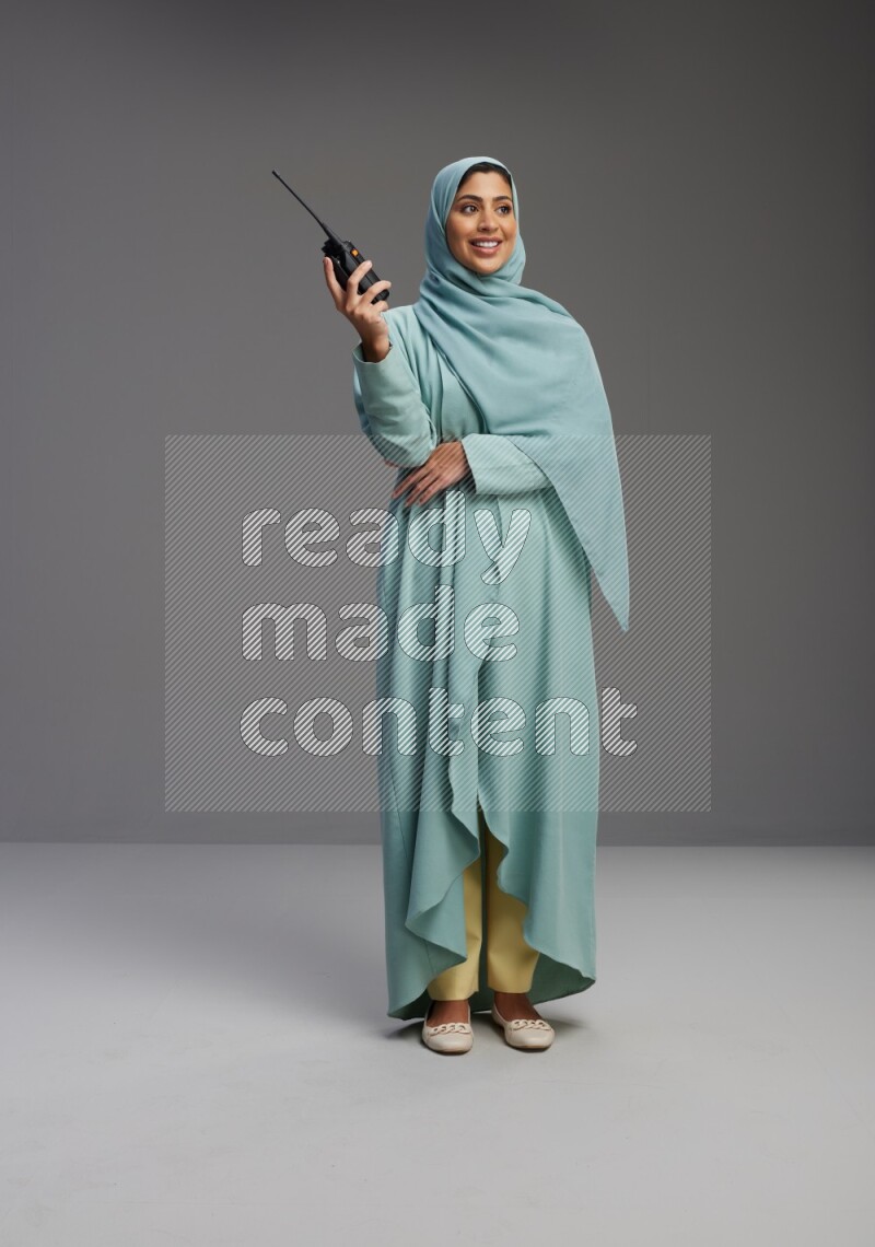 Saudi Woman wearing Abaya standing holding walkie-talkie on Gray background