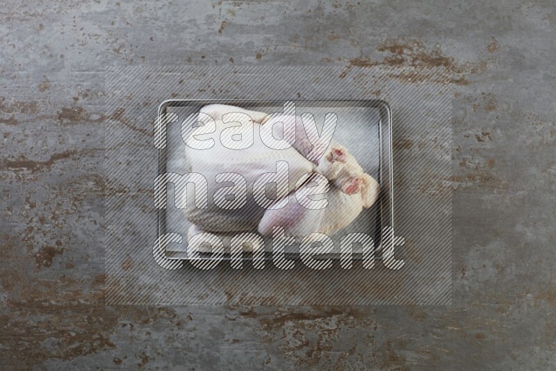 whole Raw chicken on a small oven trey direct on a rustic grey background
