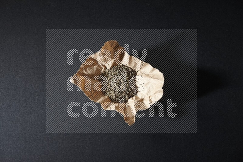 Cumin seeds in a crumpled piece of paper on black flooring