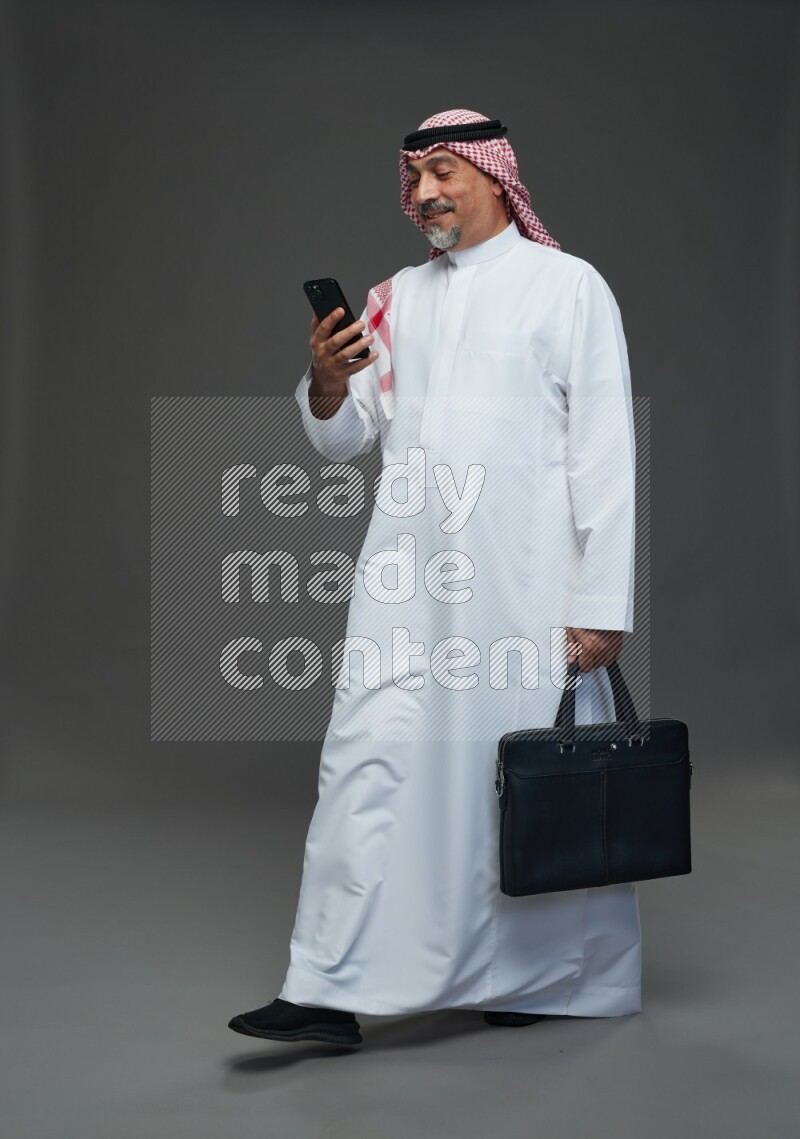 Saudi man with shomag Standing holding bag and phone on gray background