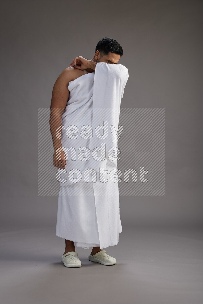 A man wearing Ehram standing showing how to sneeze on gray background