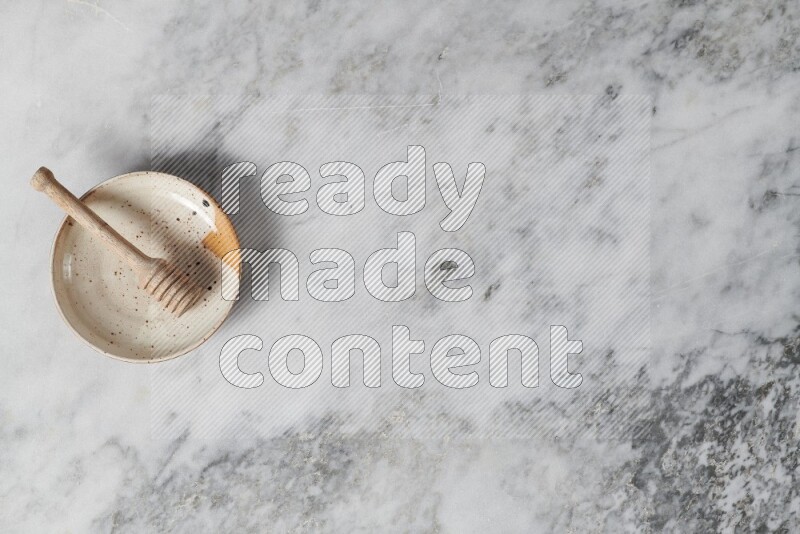 طبق فخاري متعدد الألوان مع ملعقة عسل خشبية بداخله على خلفية من الرخام الرمادي