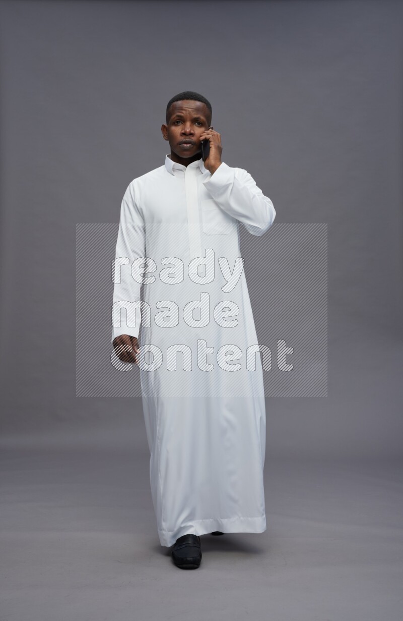 Saudi man wearing thob standing talking on phone on gray background